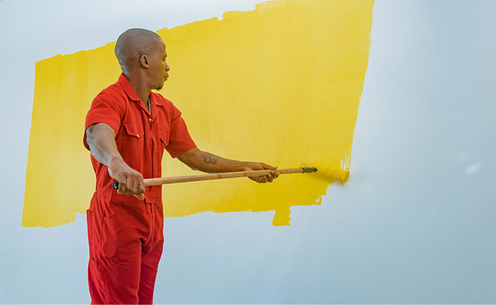 Person painting wall yellow, wearing a red jumpsuit, illustrating work-related activities linked to high earners.