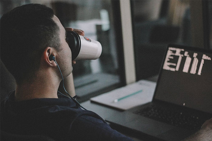 Person working on a laptop, drinking from a mug, earphones in, representing people who earn $10K and above monthly.