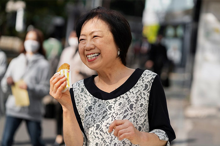 Smiling woman enjoying a snack outdoors, representing people who earn $10K and above monthly.