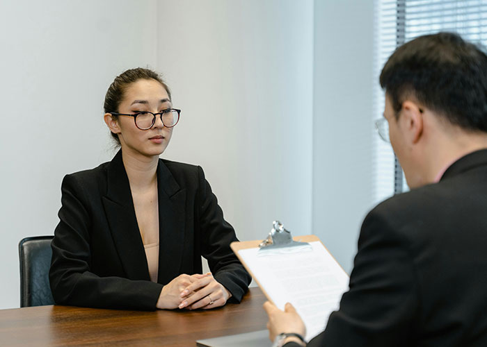 Woman in a black blazer during a job interview with a person holding a clipboard, illustrating awkward job interviews.