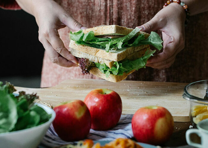 Person holding a large lettuce sandwich over a wooden board with apples nearby, showcasing life hack ideas.