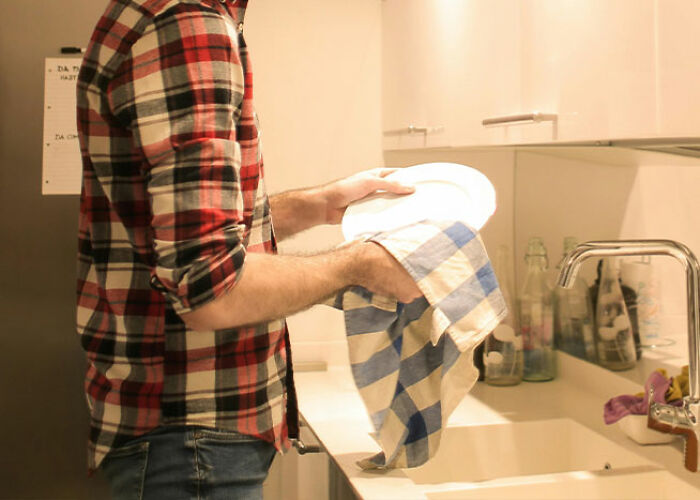 Person drying a plate in the kitchen with a blue checkered towel, demonstrating practical life hacks.