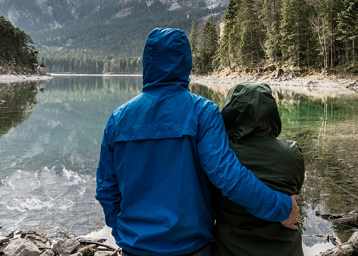Man in blue jacket hugging partner by a scenic lake, showcasing different relationship moments.