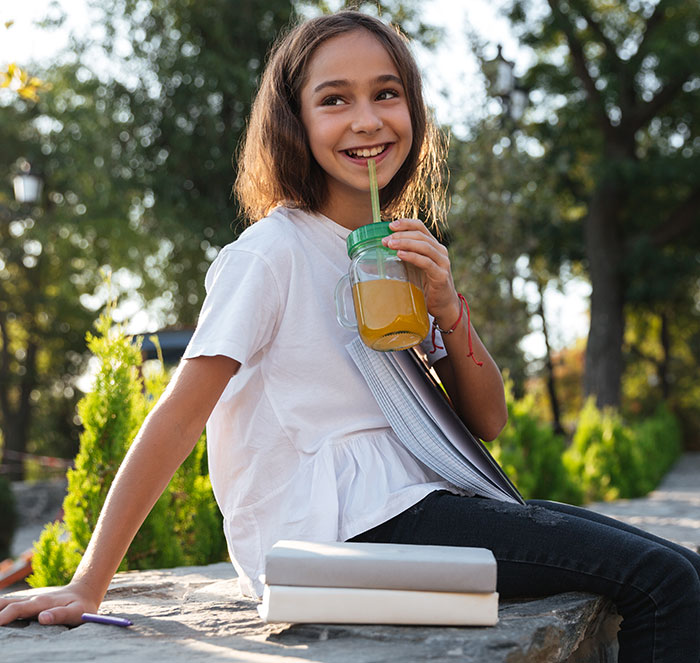 Young girl smiling while drinking a milkshake outdoors.