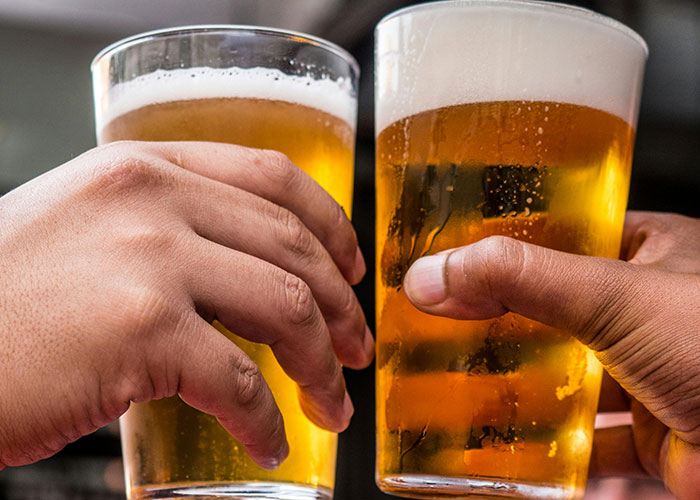 Two hands holding glasses of beer for a toast, relating to awkward job interviews.