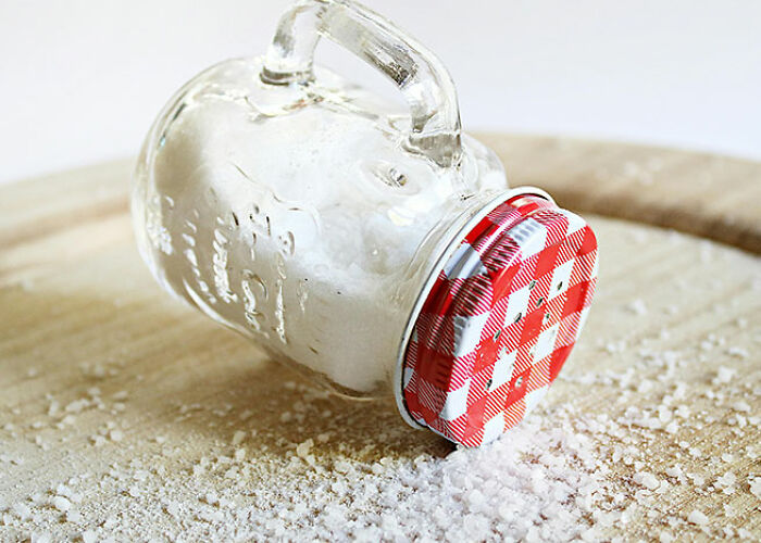 Salt shaker with a red lid lying on its side, salt spilled on a wooden surface, illustrating a life hack technique.