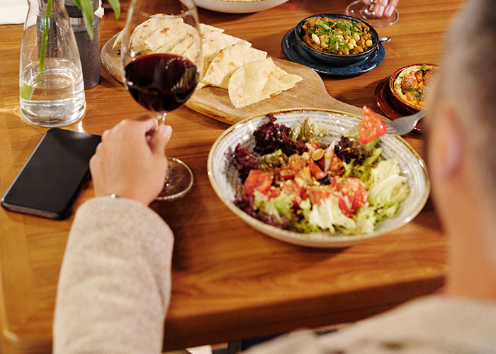 A person enjoying dinner with a salad and bread, holding a glass of red wine, reflecting a unique dining experience.