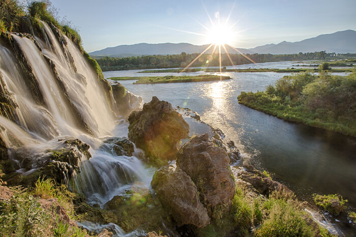 Sunset over a river with a waterfall and mountains, showcasing amazing views.