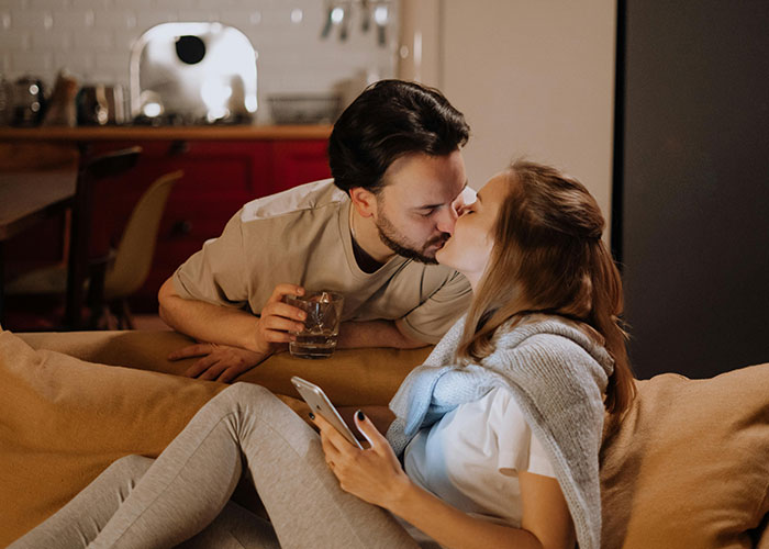A couple sharing a kiss in a cozy living room, conveying a sense of someone being different.