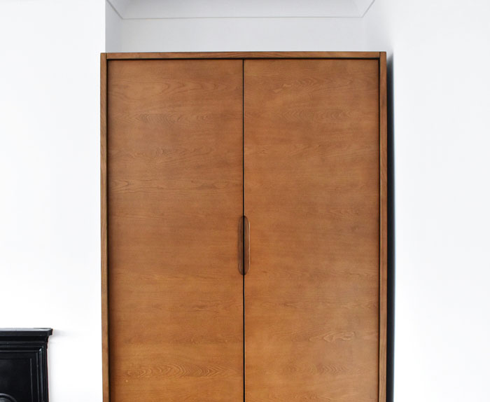 Wooden wardrobe with closed double doors in a minimalistic room symbolizing people who survived due to another’s sacrifice.