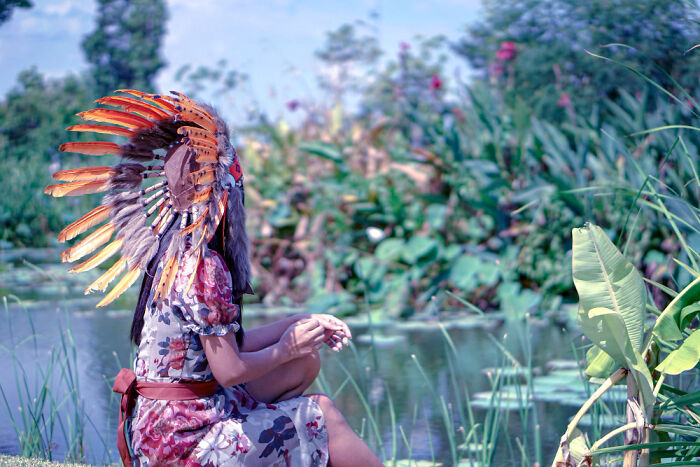 Person wearing a traditional feathered headdress sitting by a pond, illustrating facts you weren't taught in school about history.