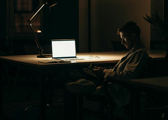 "Person sitting in dark office, illuminated by laptop screen, possibly contemplating life hacks."