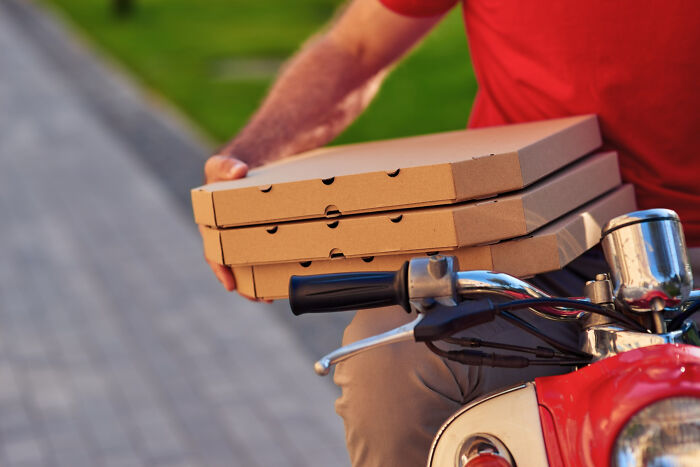 Person on a scooter delivering pizza boxes, showcasing modern technology in food delivery services.