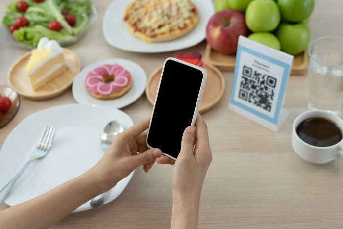 Person holding smartphone at a dining table with QR code and food, symbolizing modern technology.