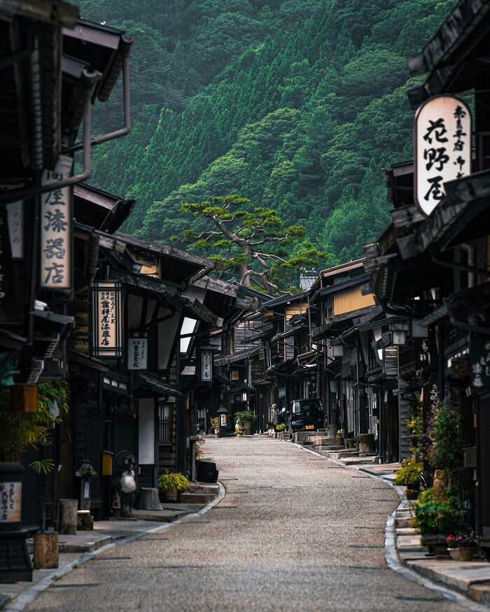 Historic Japanese street lined with traditional wooden buildings, nestled against lush green hillside.