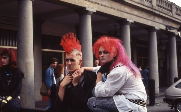 People in vibrant 80s fashion trends, with colorful mohawk hairstyles and bold makeup, in an urban setting.