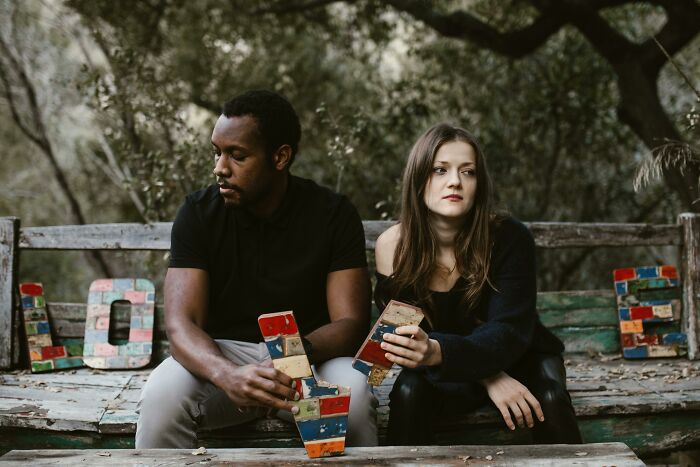A forgiving loving partner sitting on a rustic bench outdoors, holding colorful letter blocks.