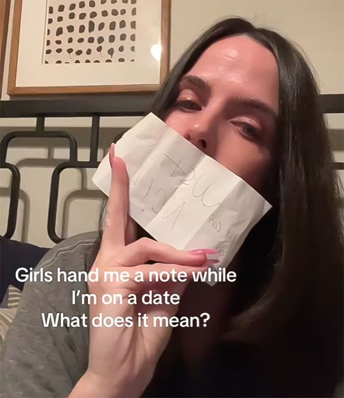 Woman with dark hair holds a note to her face, reflecting surprise during a date encounter. Woman with dark hair holds a note to her face, reflecting surprise during a date encounter.