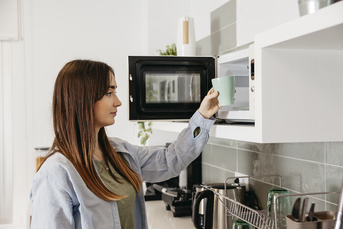 A woman using a microwave in a kitchen, illustrating how everyday things might seem harmless.