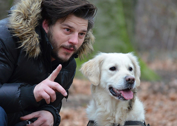 Man in a fur-trimmed jacket with a dog in a forest, showcasing something different.