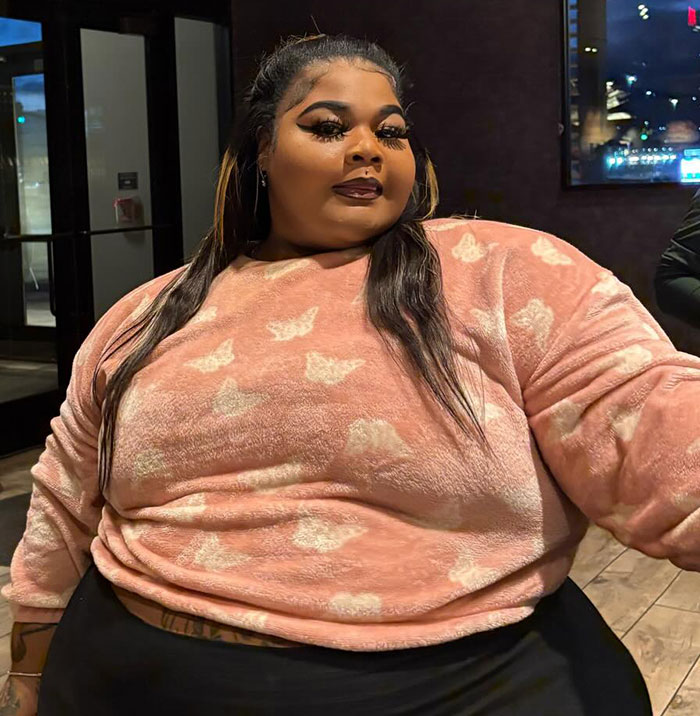 Plus size woman in a pink sweater with butterfly patterns, sitting indoors.