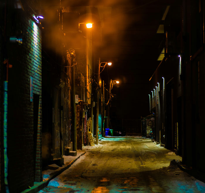 Dimly lit urban alley at night, symbolizing stories from people who survived due to another’s sacrifice.