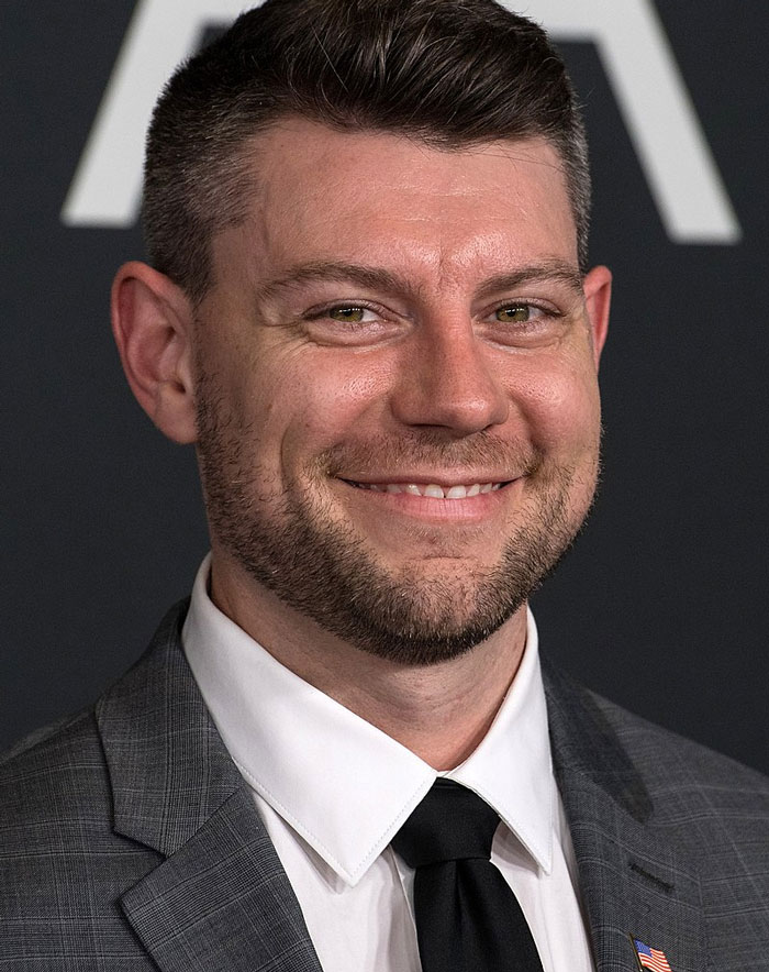 Smiling man in a suit at a formal event, representing celebrities who lost fame.