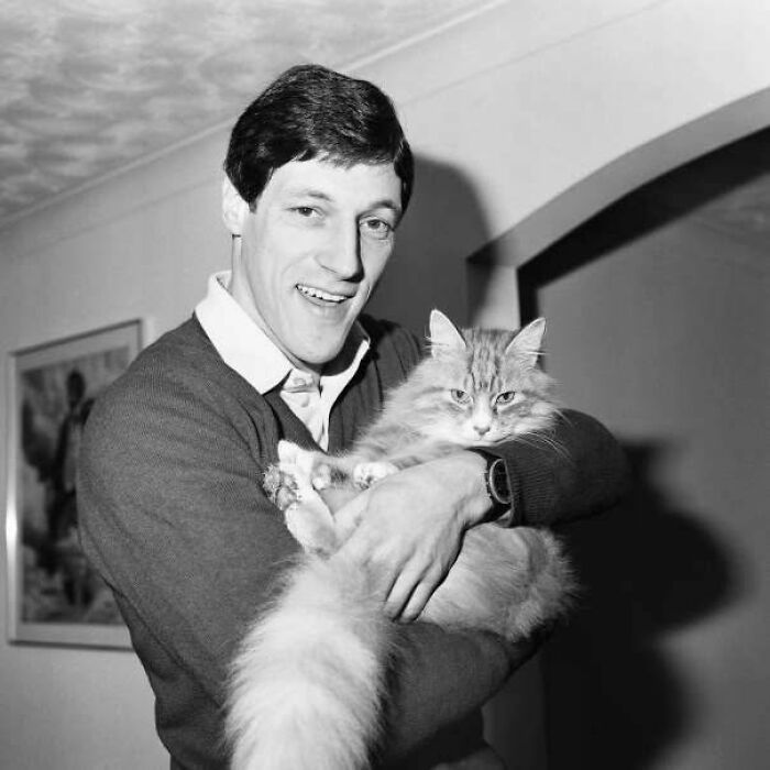 A man in a sweater holds a fluffy cat, showcasing vintage feline charm.