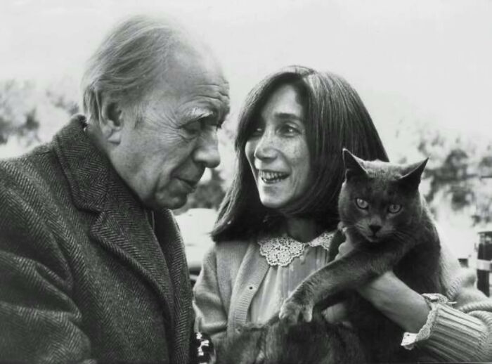 Vintage photo of a woman and older man holding a cat, highlighting timeless human-feline bonds.