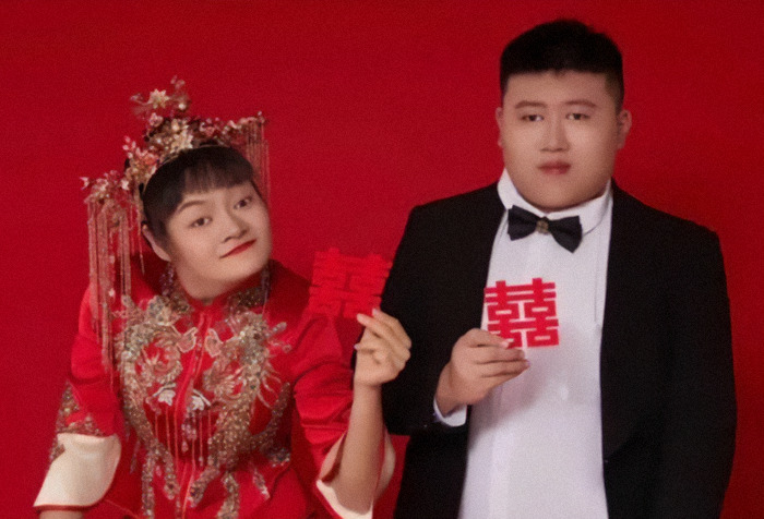 Social media star with cerebral palsy and her partner in formal attire holding Chinese celebration symbols, red background. Social media star with cerebral palsy and her partner in formal attire holding Chinese celebration symbols, red background.