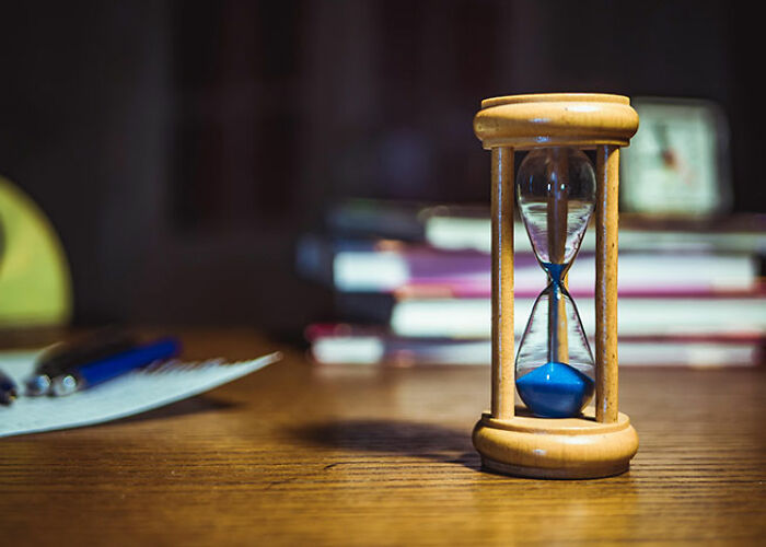 Wooden hourglass on a desk, with books and a pen, illustrating a creative life hack idea.