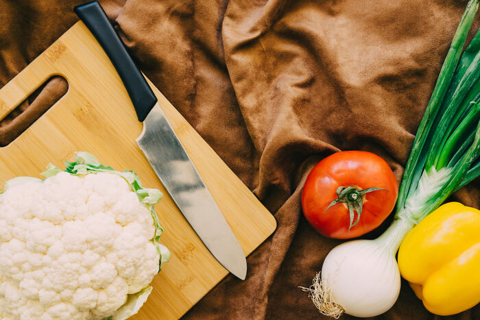 Chopping board with a knife, cauliflower, tomato, onion, and bell pepper, suggesting home cooking rules.