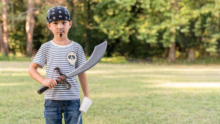 Child dressed as pirate with toy sword and mustache in a park, reflecting strict home rules theme.
