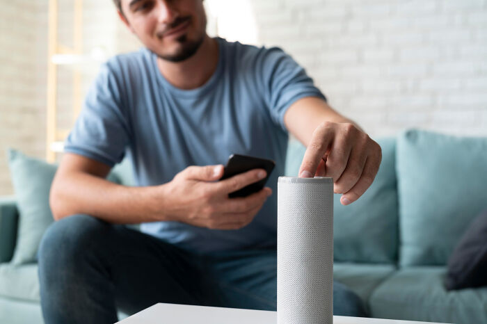 A man in a blue shirt uses a smartphone and smart speaker, symbolizing modern technology older people may refuse to use.