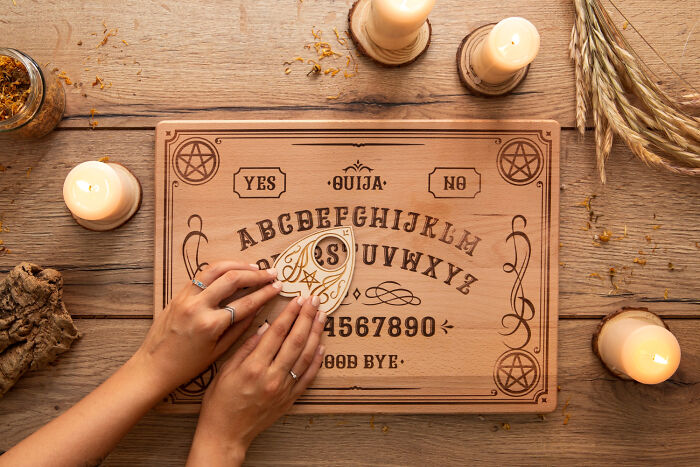 Hands using a planchette on a Ouija board, surrounded by candles, illustrating strict home rules.