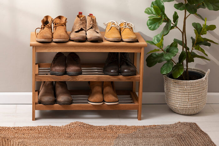 Wooden shoe rack with boots, next to a potted plant on a woven rug, showcasing a space-saving purchase.