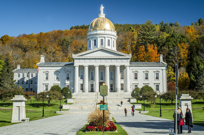 Historic white capitol building with a golden dome, surrounded by autumn trees, showcasing amazing views in states.
