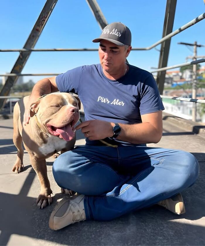 Man in blue shirt and cap sits with a pit bull on a rooftop, highlighting pit bull rescue efforts. Man in blue shirt and cap sits with a pit bull on a rooftop, highlighting pit bull rescue efforts.