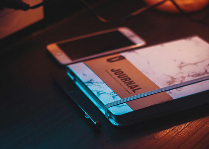 Journal with a smartphone and pen on a desk, illuminated by ambient lighting.