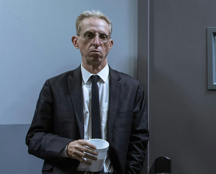 Man in a suit with a stern expression holding a paper cup, related to police officer corruption discussion.