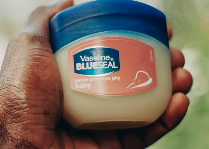 Hand holding a jar of Vaseline Blue Seal, a life hack product for skincare.
