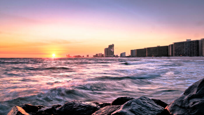 Sunset over ocean and city skyline offering amazing views with rocky shoreline in the foreground.