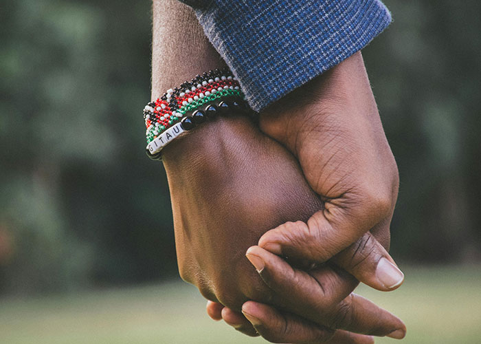 Two hands holding, one wearing beaded bracelets, conveying connection and a sense of being different.