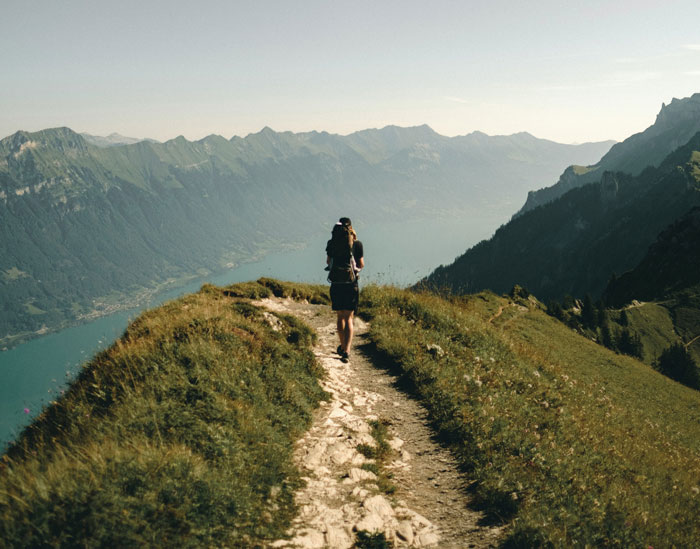 Person hiking on a scenic mountain trail overlooking a lake, related to unsolved true crime cold cases.