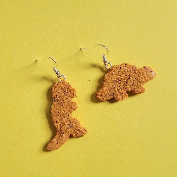 Mismatched cookie dinosaur earrings on a yellow background.