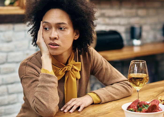 Woman reflecting with a glass of wine on table, responding to boyfriend's inappropriate comment. Woman reflecting with a glass of wine on table, responding to boyfriend's inappropriate comment.