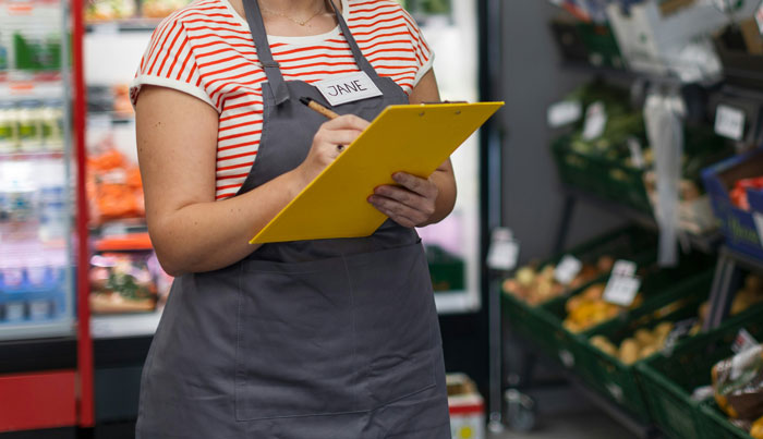 Walmart employee holding a clipboard in a grocery aisle.