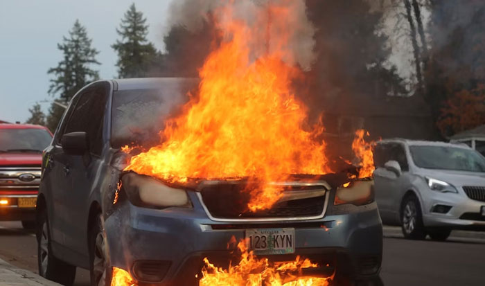 Car engulfed in flames on a street, illustrating people who survived due to another’s sacrifice in a dramatic accident.