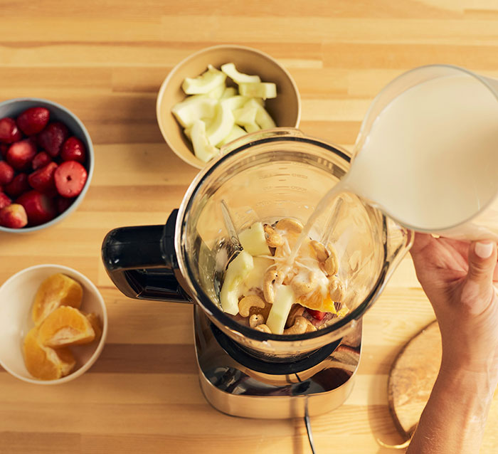 Milkshake preparation using blender with fruits and milk.