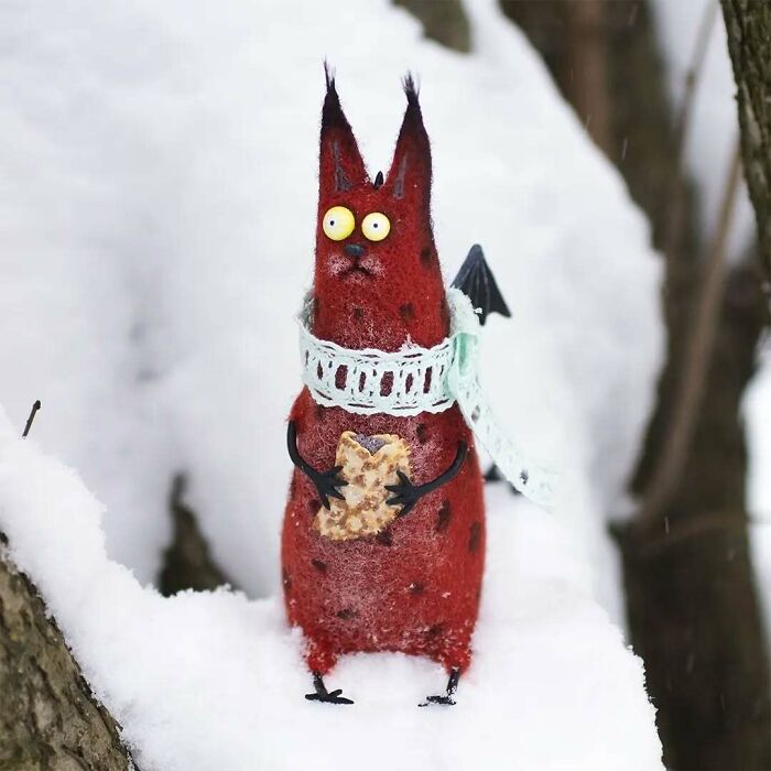 Strange art doll of a funny-looking red animal with yellow eyes and a scarf, standing on snow.